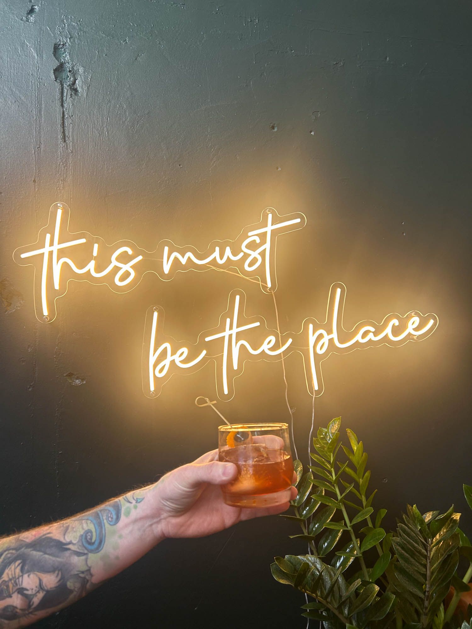 A hand holding a drink and neon lights on the wall.